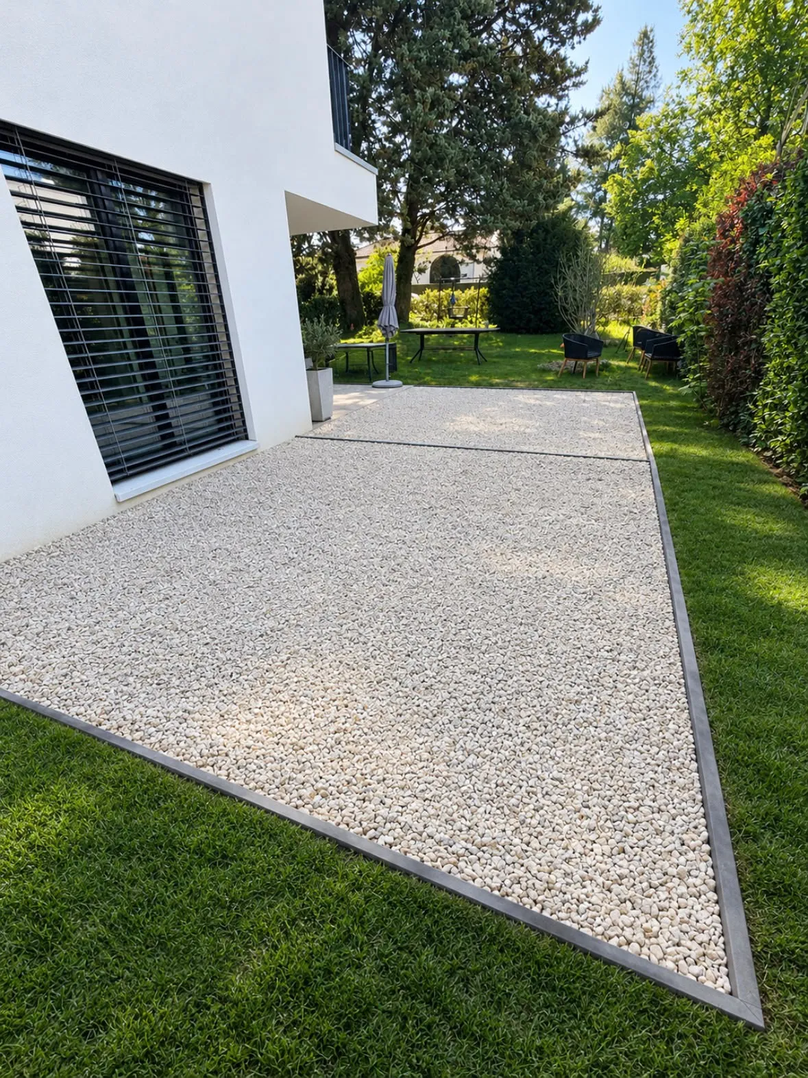 Terrasse en gravier clair bordée de profilés métalliques le long d’une villa